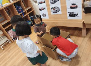 Students creating a car using a large cardboard box