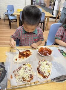 Little boy spreading tomato sauce on some pizza dough