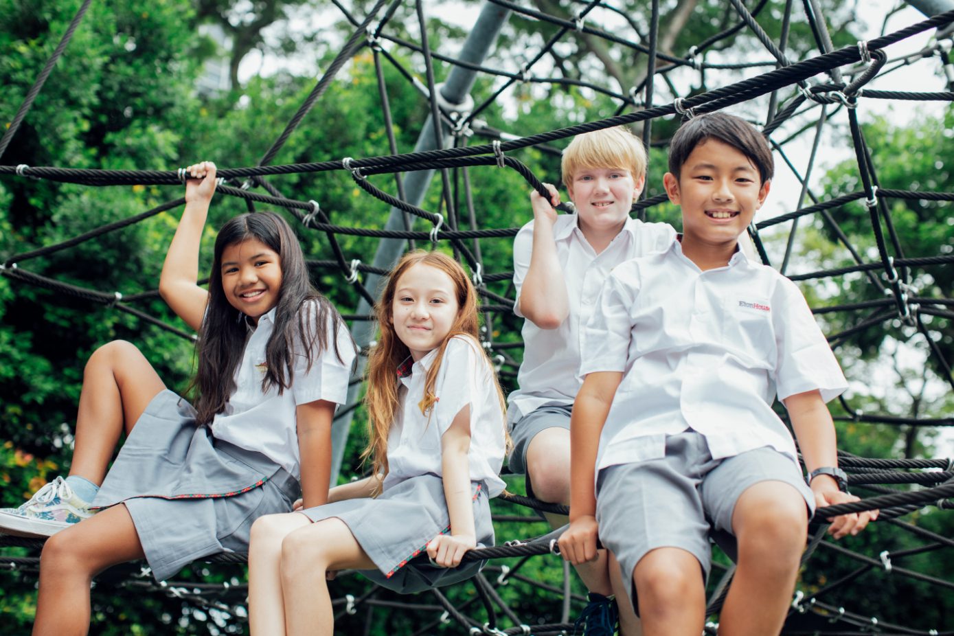 Four EtonHouse Broadrick children smiling together on the playground climbing net
